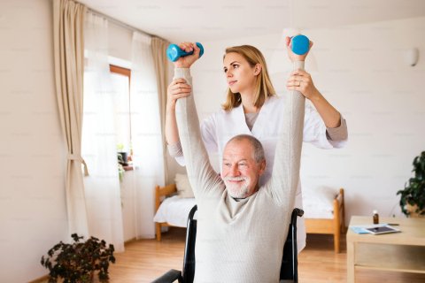 Senior man in wheelchair being assisted with arm exercises by a nurse